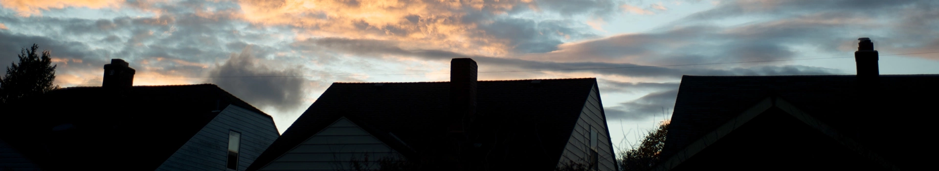 trzy dachy z kominami na tle zachodzącego słońca